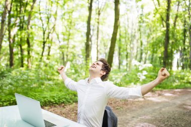 Mutlu çıktıktan iş adamı kaldırdı elleriyle kutlamak büyük iş veya Ofis Masası yeşil park laptop önünde harika bir haber. İş kavramı.