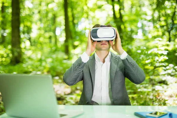 stock image Confident handsome business man with virtual reality glasses pointed with finger at office desk in green park. Business concept.