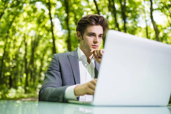 Ritratto di pensiero Uomo d'affari seduto alla scrivania dell'ufficio lavora al computer portatile nel parco verde della foresta. Libero professionista con le mani sul mento che lavora sul tavolo da ufficio nel parco verde. Ritratto aziendale . — Foto Stock