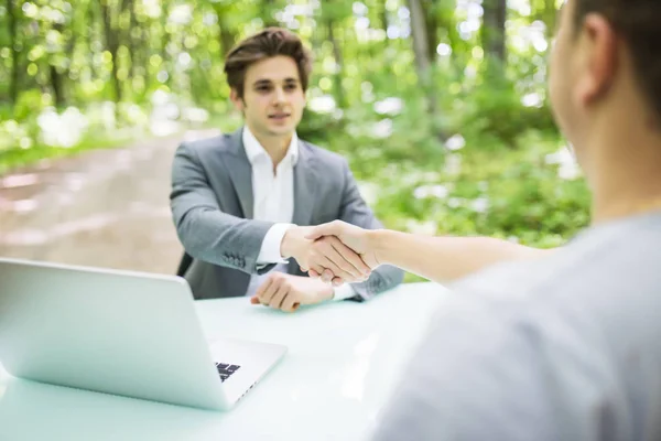 Gestionnaire en costume accueille avec poignée de main lors de l'entrevue nouvel homme ouvrier à sa table de bureau dans la forêt de parc vert. Concept d'entreprise . — Photo