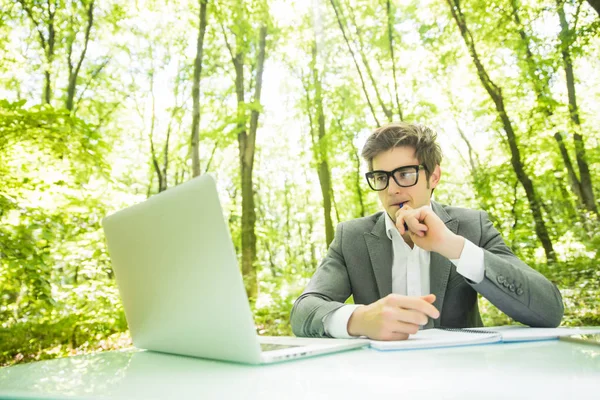 Ritratto di giovane bell'uomo d'affari in giacca e cravatta che lavora al computer portatile al tavolo dell'ufficio nel parco verde della foresta. Concetto aziendale . — Foto Stock