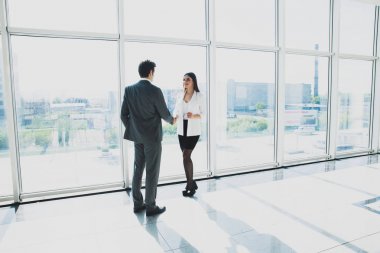 modern ofis panoramik pencerelere ile iki genç iş adamı ve iş kadını ayakta.