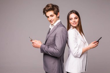 Genç çift akıllı telefonlar kullanarak ve üzerinde gri bir arka arkaya dururken gülümseyerek. Kameraya bak.