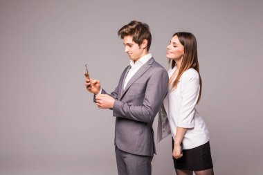 Genç çift akıllı telefonlar kullanarak ve üzerinde gri bir arka arkaya dururken gülümseyerek. Kadın adama bakın.