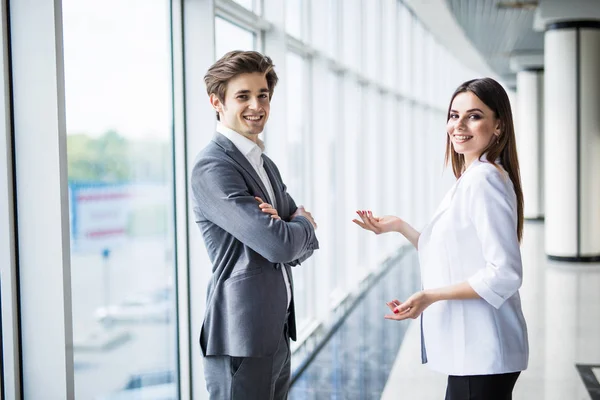 Business men and women talking with a smile on the background of the large panoramic windows in a modern business center. Models dressed in a dark business suits. — Stock Photo, Image