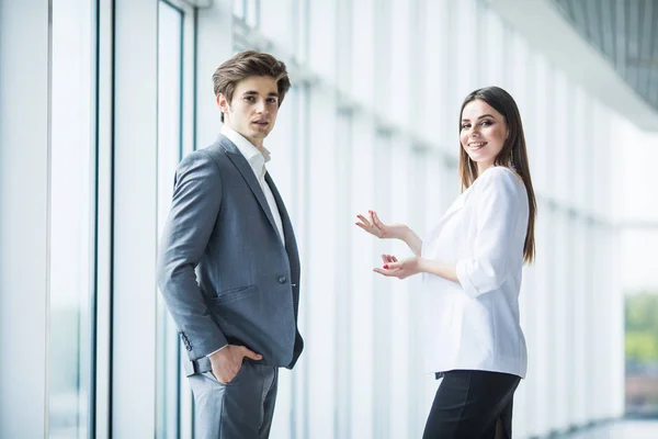 Business, teamwork, partnership, cooperation and people concept - business people talking each other over panoramic office windows. Business man and business woman in office — Stock Photo, Image
