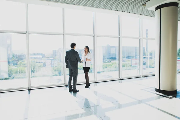 Deux jeunes hommes d'affaires et femmes d'affaires sont debout dans un bureau moderne avec des fenêtres panoramiques . — Photo