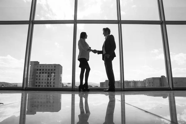 Silueta de hombre de negocios y mujer de negocios estrechando la mano en la oficina con grandes ventanas panorámicas, concepto de negocio . — Foto de Stock