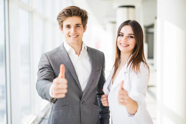 Motivated businessman and woman giving a thumbs up gesture of approval and success as they pose side by side giving the camera big friendly enthusiastic smiles — Stock Photo, Image