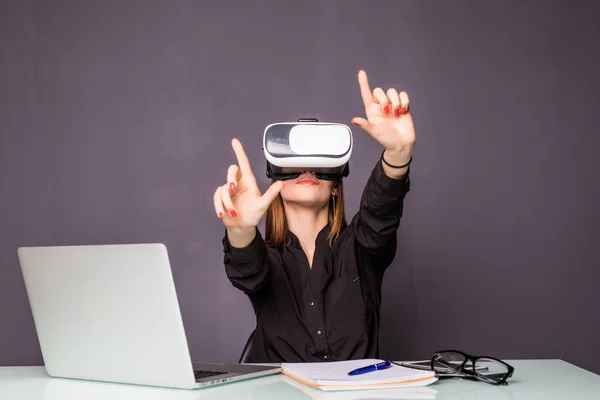 Mujer con gafas VR. Mujer joven y segura con auriculares de realidad virtual apuntando en el aire mientras está sentada en su lugar de trabajo en la oficina — Foto de Stock