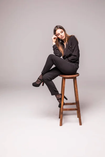 Skönhet kvinna sitter på en stol över grå bakgrund — Stockfoto