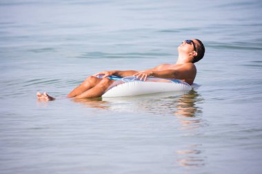 Bir bardak bira kauçuk halka okyanus su üzerinde yüzen ile güneş gözlüklü genç adam