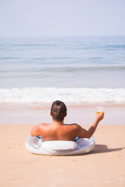 Yakışıklı adam deniz sahilde kauçuk halka tarihinde tabaklanmış ve bir bardak soğuk bira içmek ve yaz meslek tadını çıkarın