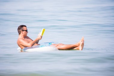 Genç adam sakin ol şişme halka bir kitap okumak okyanus su içinde. Yaz meslek