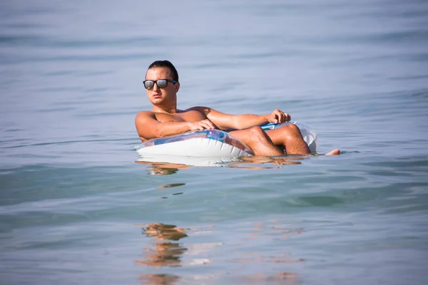 Красивый молодой человек, плавающий на надувном кольце в морской воде и расслабляющий в летнем призвании — стоковое фото