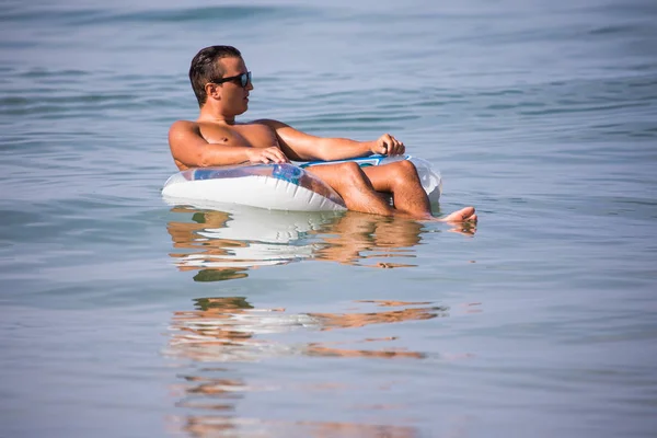 Gelukkig jongeman ontspannen in het water van de Oceaan op rubberring en geniet van de zomer roeping. — Stockfoto