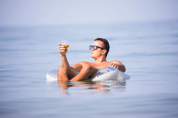 Man relax in the ocean water on rubber ring drink beer and enjoy summer vocation. — Stock Photo, Image