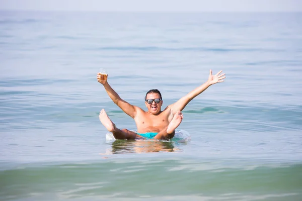 Красивый мужчина, плавающий на резиновом кольце в море со стаканом пива и праздничным настроением, наслаждается летним призванием — стоковое фото