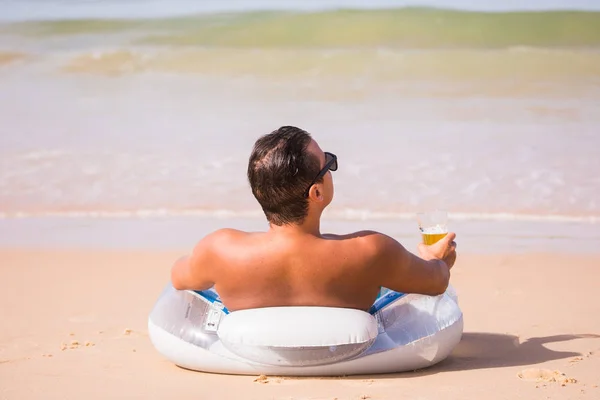 Kjekken mann solbrent på gummilingen på stranden, drakk et glass kaldt øl og nøt sommerens kall – stockfoto