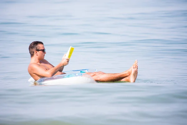 Jonge man in ontspannen in het water van de Oceaan op opblaasbare ring een boek lezen. Zomer roeping — Stockfoto