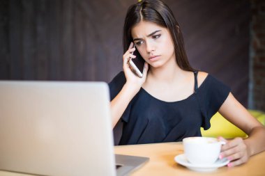 Kafede masada bir dizüstü bilgisayar ile telefonda konuşurken üzgün genç kadın
