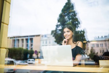 Pencere cam göz sırasında bir kafede bir bilgisayarda çalışan kadın.