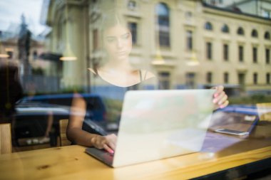 Pencere cam göz sırasında bir kafede bir bilgisayarda çalışan kadın.