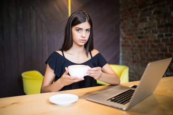 Ung kvinna dricka kaffe och använder dator på café — Stockfoto