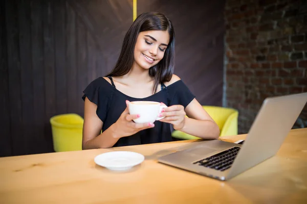 Junge Frau trinkt Kaffee und benutzt Computer im Café — Stockfoto