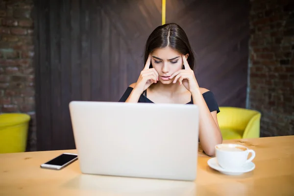 Retrato de una mujer joven pensando en algo mientras está sentada frente a la computadora portátil portátil en el interior de la cafetería moderna, hermosa mujer de ensueño tomando un descanso entre el trabajo en el net-book durante el desayuno — Foto de Stock