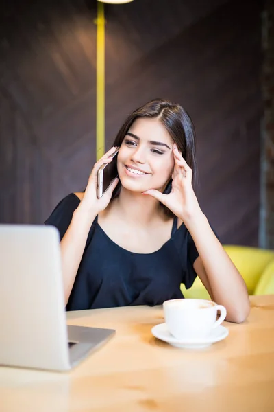 Smile Young woman talking on the phone with a laptop on table in cafe — Stock Photo, Image