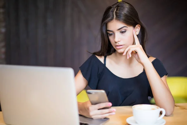 Elegant ung kvinna med en bärbar dator på ett kafé med en mobiltelefon . — Stockfoto