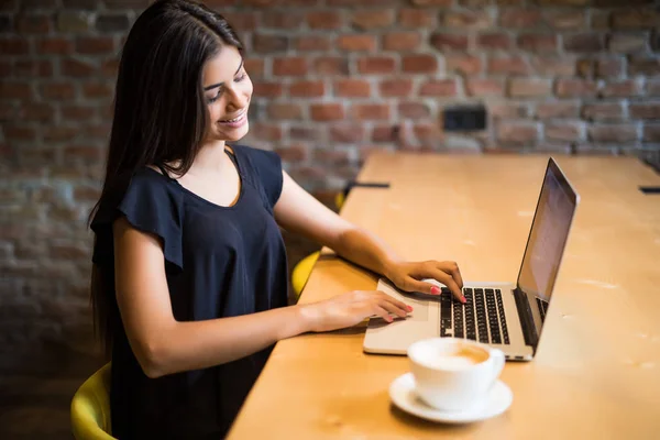 Side view of a female student using laptop at cafeteria table and typing — Stock Photo, Image