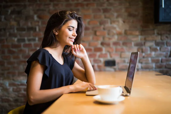Mujer joven e independiente sentada en la cafetería con laptop y tomando café. Mujer joven con portátil en la cafetería . — Foto de Stock