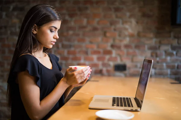 Joven hermosa mujer bebiendo café en el bar de la cafetería delante de la computadora portátil . — Foto de Stock