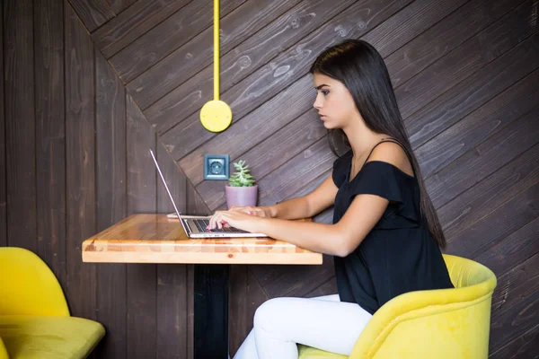 Yaratıcı office veya kafe pencere yanında otururken dizüstü bilgisayarda çalışan akıllı rahat kıyafet kendine güvenen genç kadın