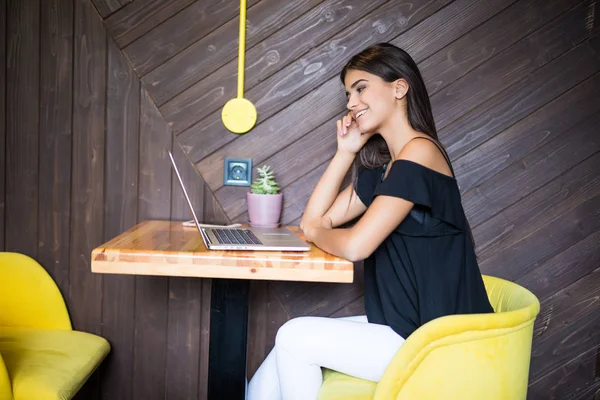 Yaratıcı office veya kafe pencere yanında otururken dizüstü bilgisayarda çalışan akıllı rahat kıyafet kendine güvenen genç kadın