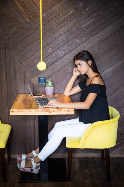 Yaratıcı office veya kafe pencere yanında otururken dizüstü bilgisayarda çalışan akıllı rahat kıyafet kendine güvenen genç kadın