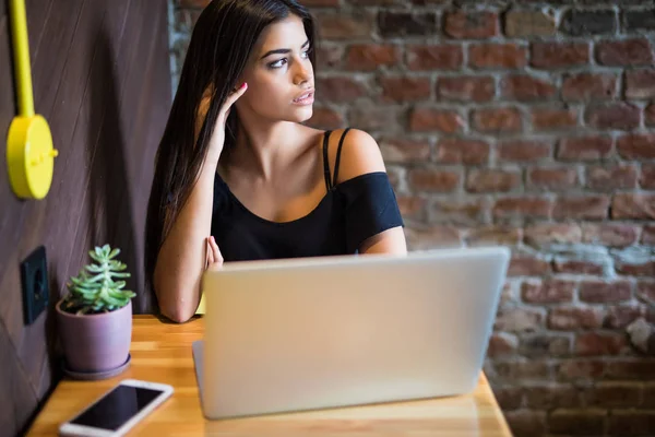 Hermosa mujer caucásica soñando con algo mientras está sentada con netbook portátil en el moderno bar de la cafetería, joven y encantadora freelancer mujer pensando en nuevas ideas durante el trabajo en el ordenador portátil — Foto de Stock