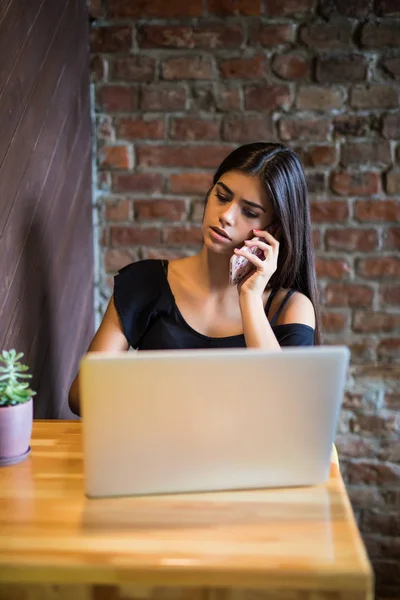 Ung kvinna talar i mobiltelefon och använda laptop i café — Stockfoto