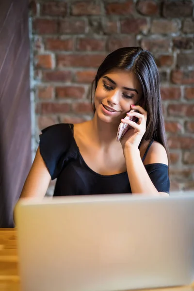 Mujer joven hablando en el teléfono celular y el uso de ordenador portátil en la cafetería — Foto de Stock