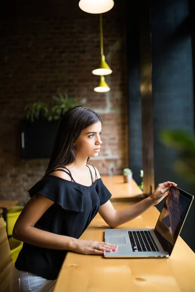 Oldalnézet. Fiatal nő ül asztal notebook kávézó és teszi a megjegyzésekben. Online tanulás. Diák csinál házi feladatot. — Stock Fotó