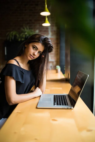 Vista lateral. Mujer joven sentada en la mesa en la cafetería y toma notas en el cuaderno. Aprendizaje online. Estudiante haciendo tarea . — Foto de Stock