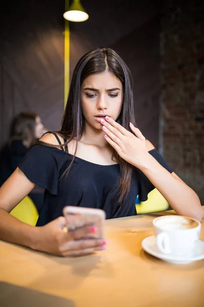 Closeup portrait anxious young girl looking at phone seeing bad news or photos with disgusting emotion on her face isolated cafe background. Human emotion, reaction, expression — Stock Photo, Image