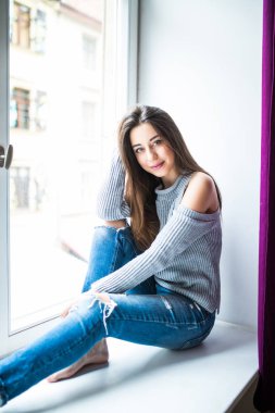 Güzel bir genç kadın evde pencere kenarında oturuyor.