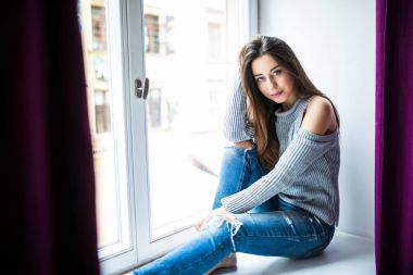 Güzel bir genç kadın evde pencere kenarında oturuyor.