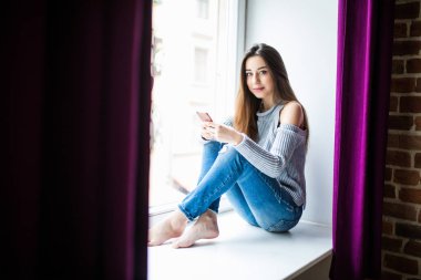 pencere pervazına siting elinde cep telefonu olan kadın