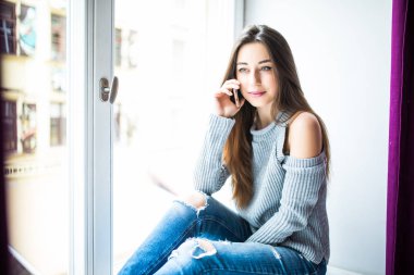 Pencere pervazına üzerinde oturan telefonla konuşurken ile güzel kız.
