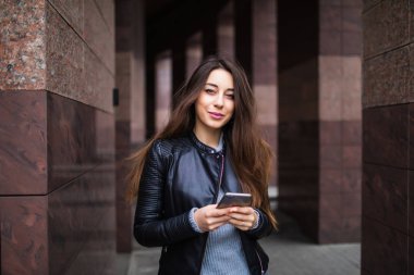 güzel genç kadın bir app onun smartphone aygıt bina arka plan önünde bir kısa mesaj göndermek için kullandığı