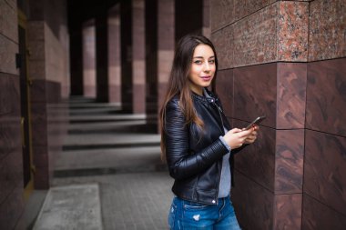 Ofis binaları içinde belgili tanımlık geçmiş ile bir akıllı telefon kullanan genç kadın